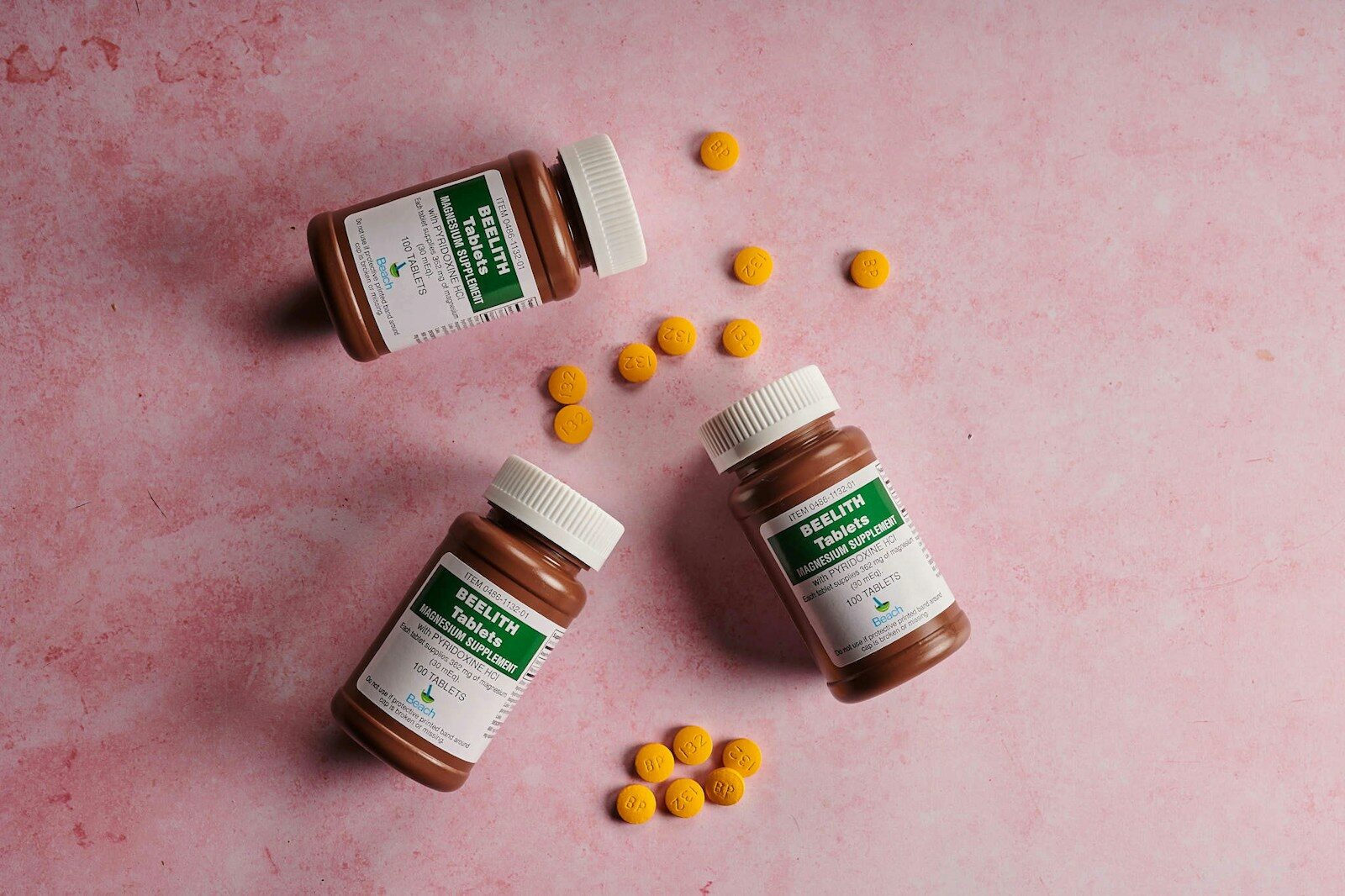three bottles of vitamin pills on a pink surface