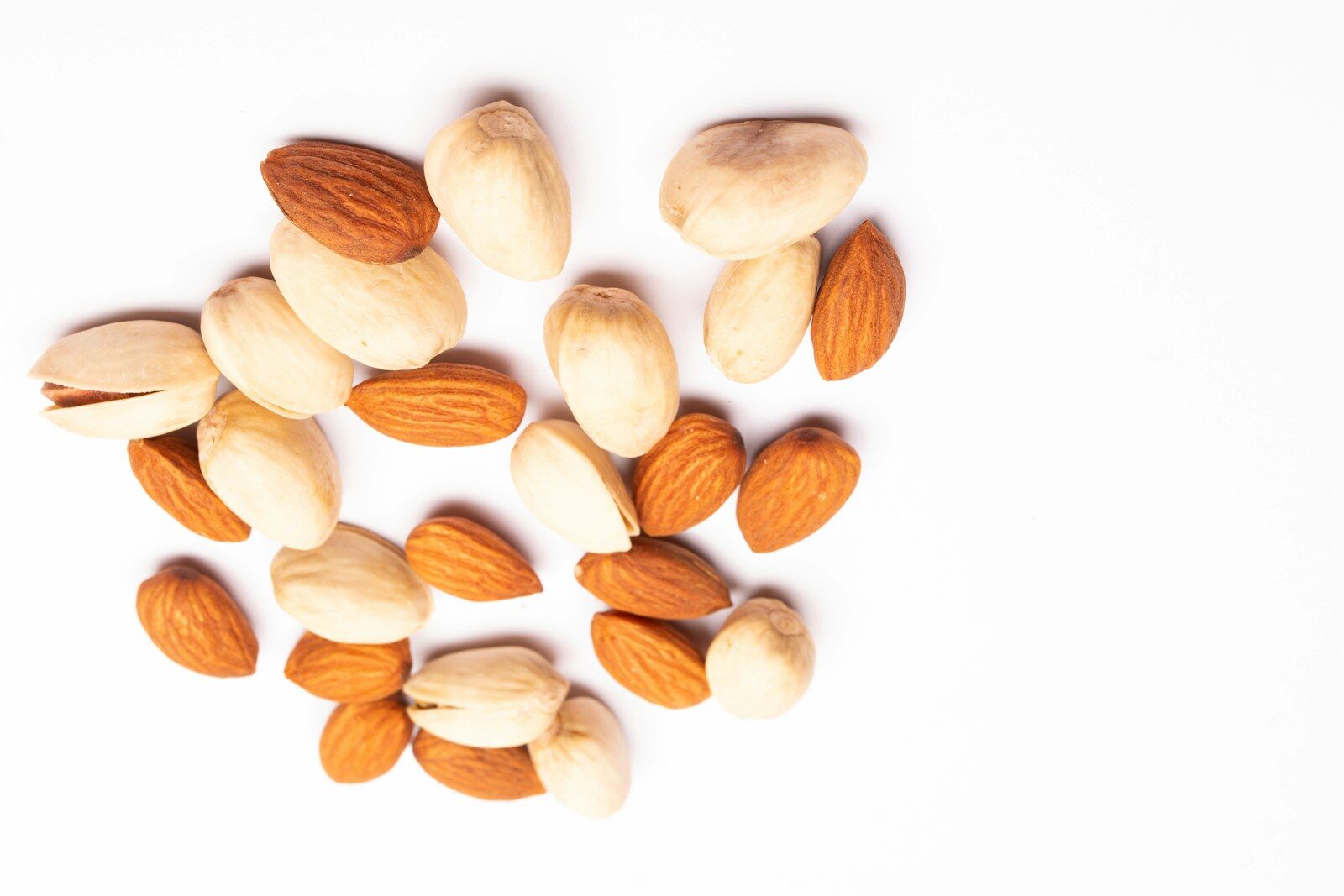 A pile of almonds and pistachios on a white background.