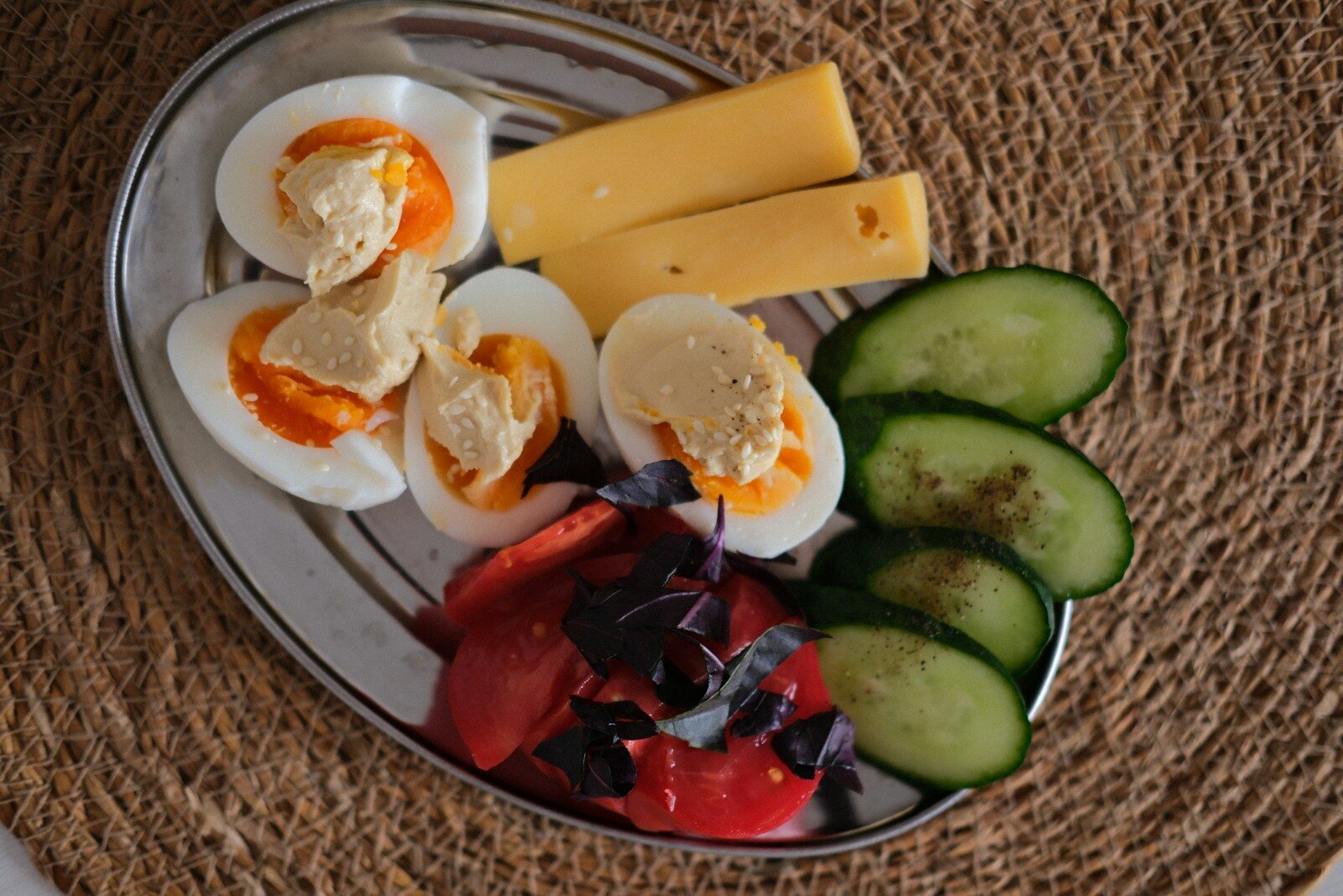 Plate with deviled eggs, cheese, sliced cucumber, and tomato.