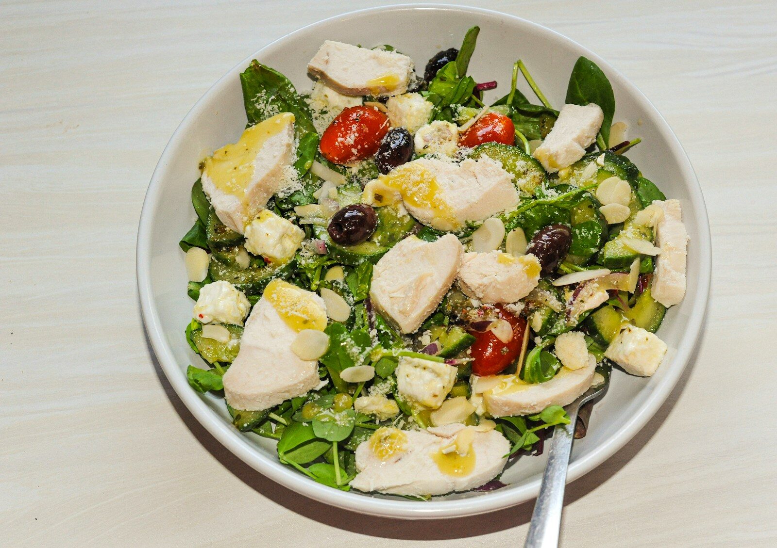 A chicken salad with spinach, tomatoes, olives, feta, and almonds in a bowl